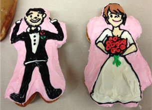 Two Doughnuts shaped and frosted to look like a traditional groom and bride