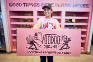Close up shot of pink Voodoo Doughnut box held by a woman in the background
