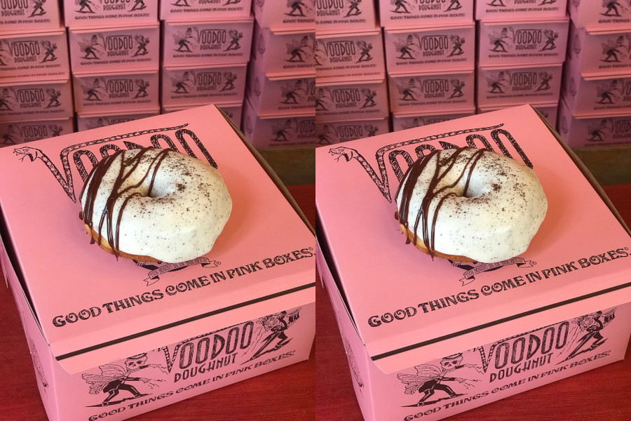 Doughnut with white icing and chocolate drizzle on a pink Voodoo Doughnut box.