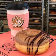 Nossa Familia Coffee and Doughnut coffee cup with Voodoo Logo and Nossa Familia Coffee Doughnut sitting on a pink doughnut box