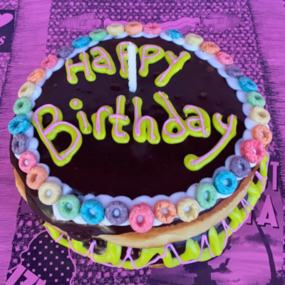 Two stacked doughnuts iced in chocolate with the words Happy Birthday and a single candle.