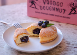 Doughnut on a plate cut open with blueberry filling and pink box in background