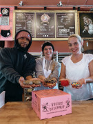 Man and two women holding doughnuts over a pink box