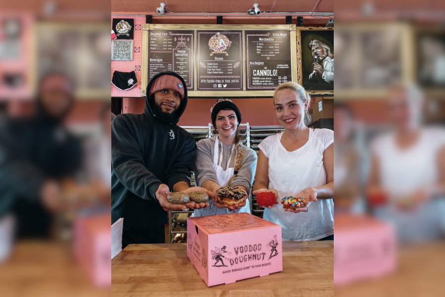 Man and two women holding doughnuts over a pink box