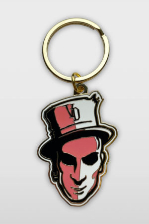 Metal keychaing showing a face with a tophat in pink and gold