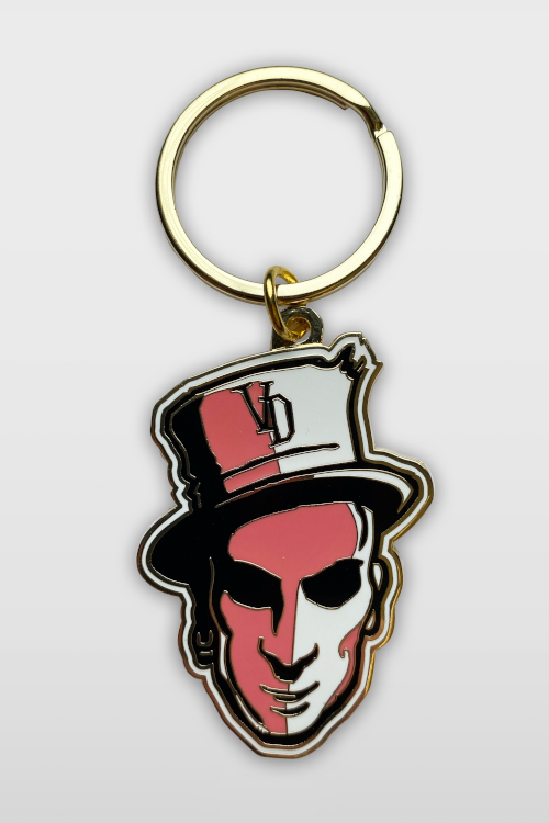 Metal keychaing showing a face with a tophat in pink and gold