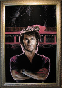 Patrick Swayze with arms crossed in front of a Voodoo Doughnut Storefront. In Black Velvet